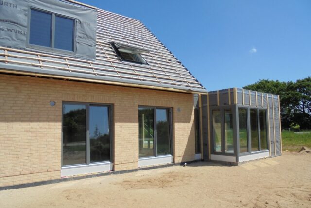 Hausdach mit Schleppgaube und Dachfenster, daneben ein Anbau mit Glasfront während der Bauarbeiten