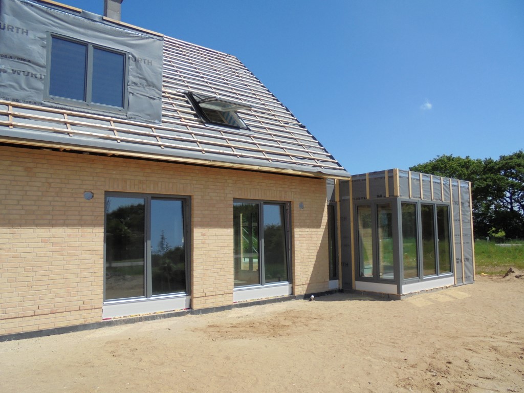 Hausdach mit Schleppgaube und Dachfenster, daneben ein Anbau mit Glasfront während der Bauarbeiten